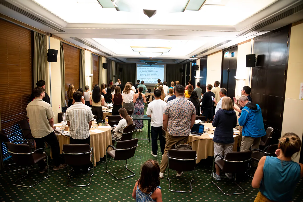 The group standing together to sing in a meeting room