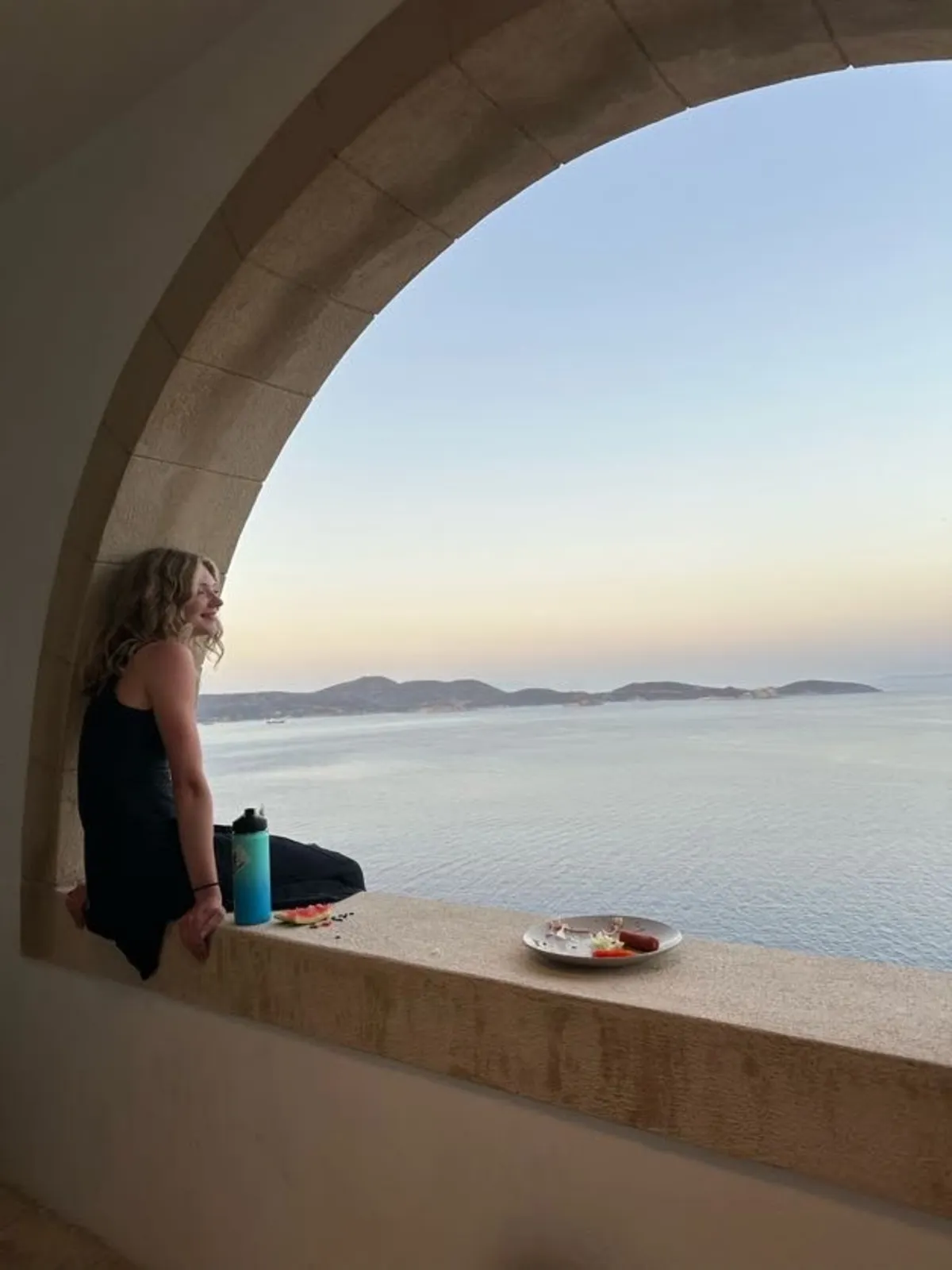 A student sitting in an arched window looking out over the sea