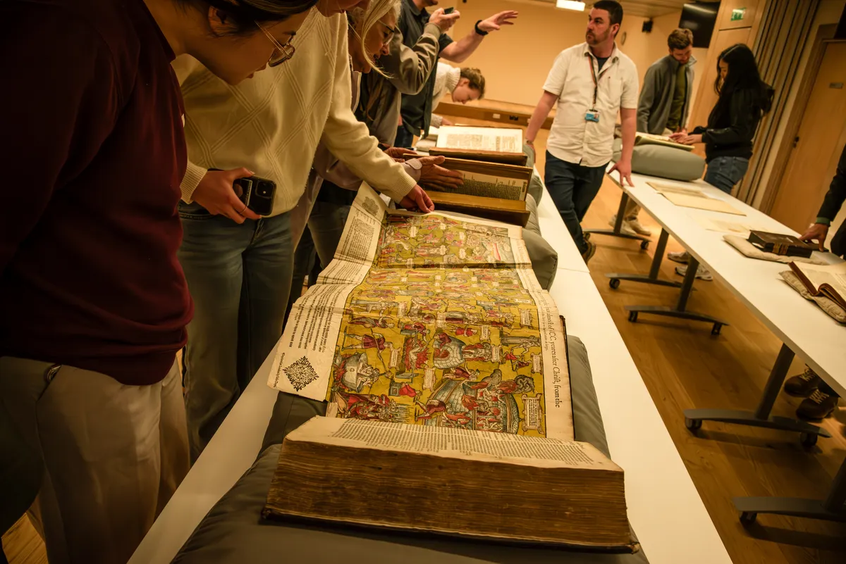 Students leaning over an illuminated folio in a library
