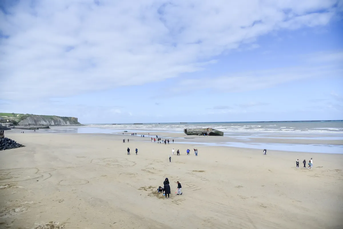 A wide Normandy beach with the group scattered across the sand