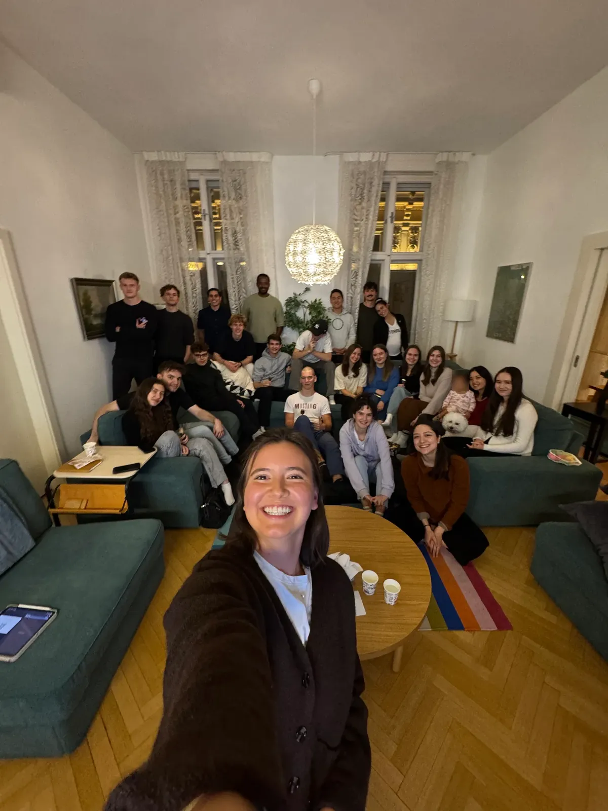 A living room of students, one leaning in for a selfie