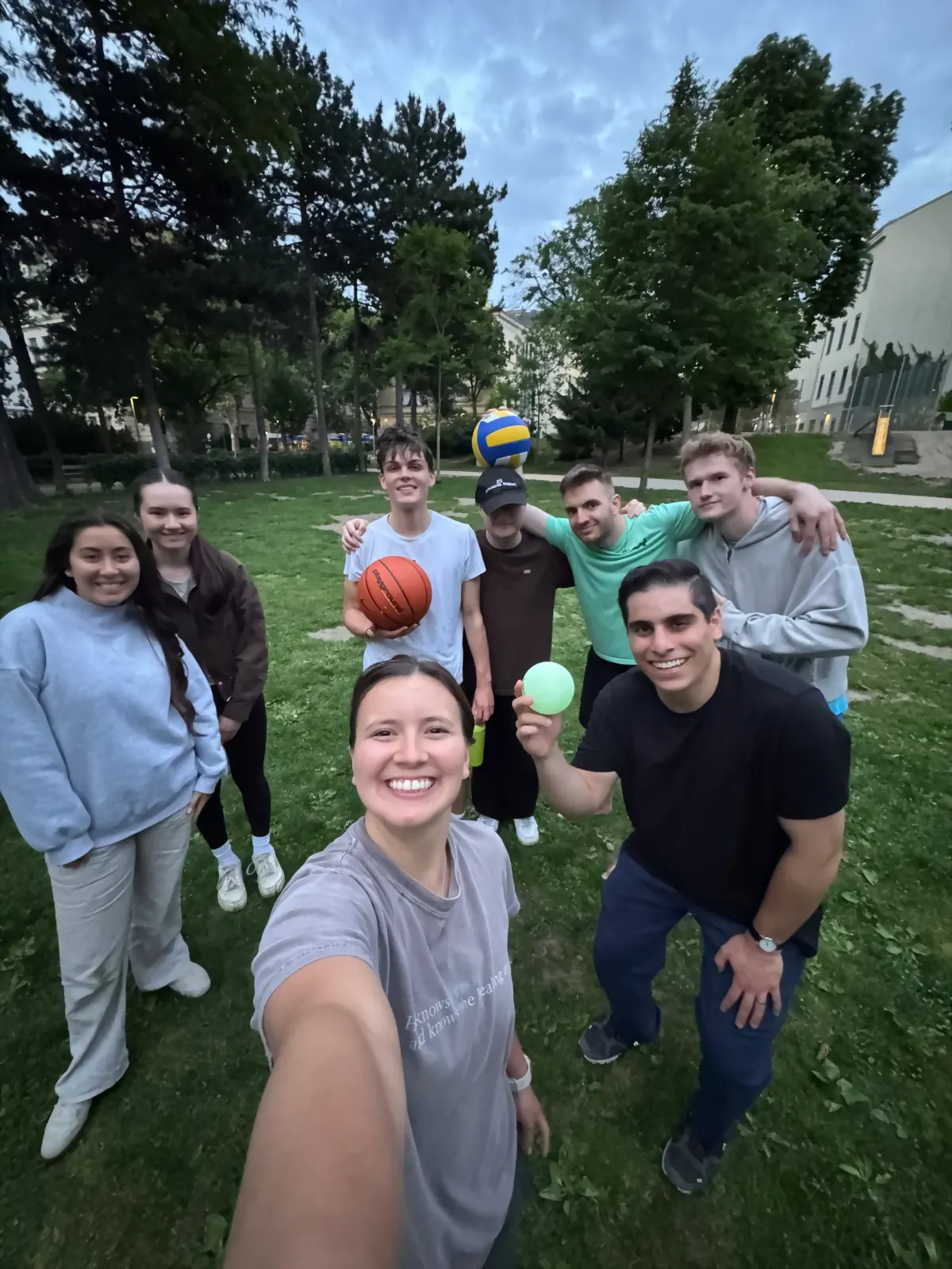 Students outdoors at dusk with basketballs and a volleyball