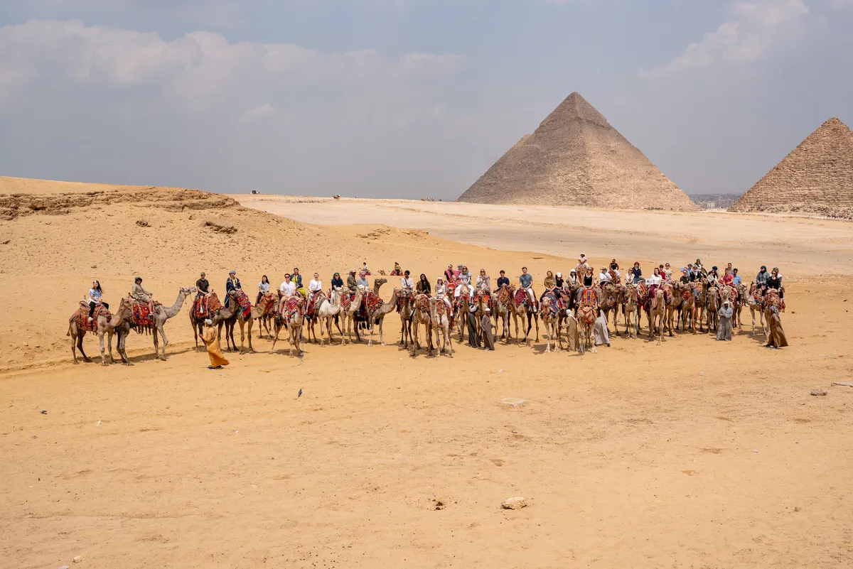 Camel riders crossing the sand at the Pyramids of Giza